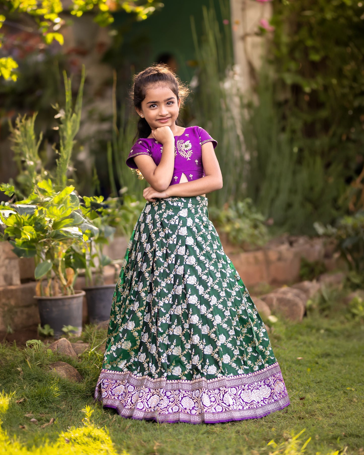 A DARK GREEN JAAL BANARASI LEHENGA WITH PURPLE RAW SILK BLOUSE.